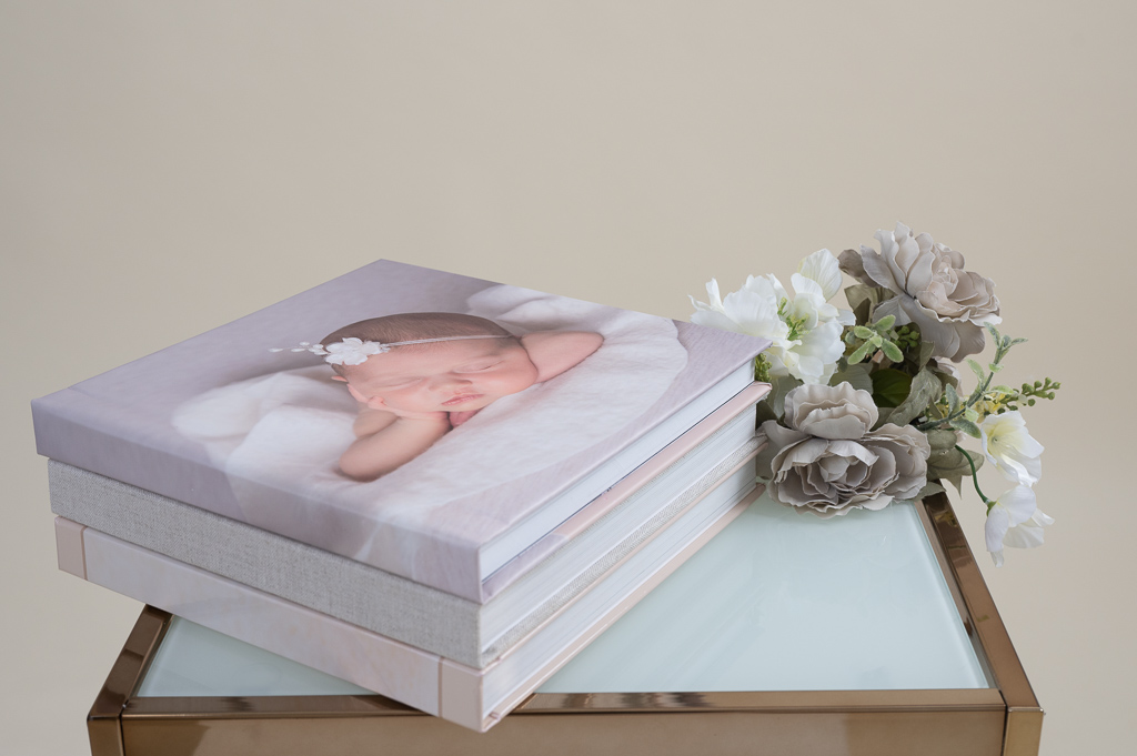 three stacked baby albums on glass table. flowers decorating.