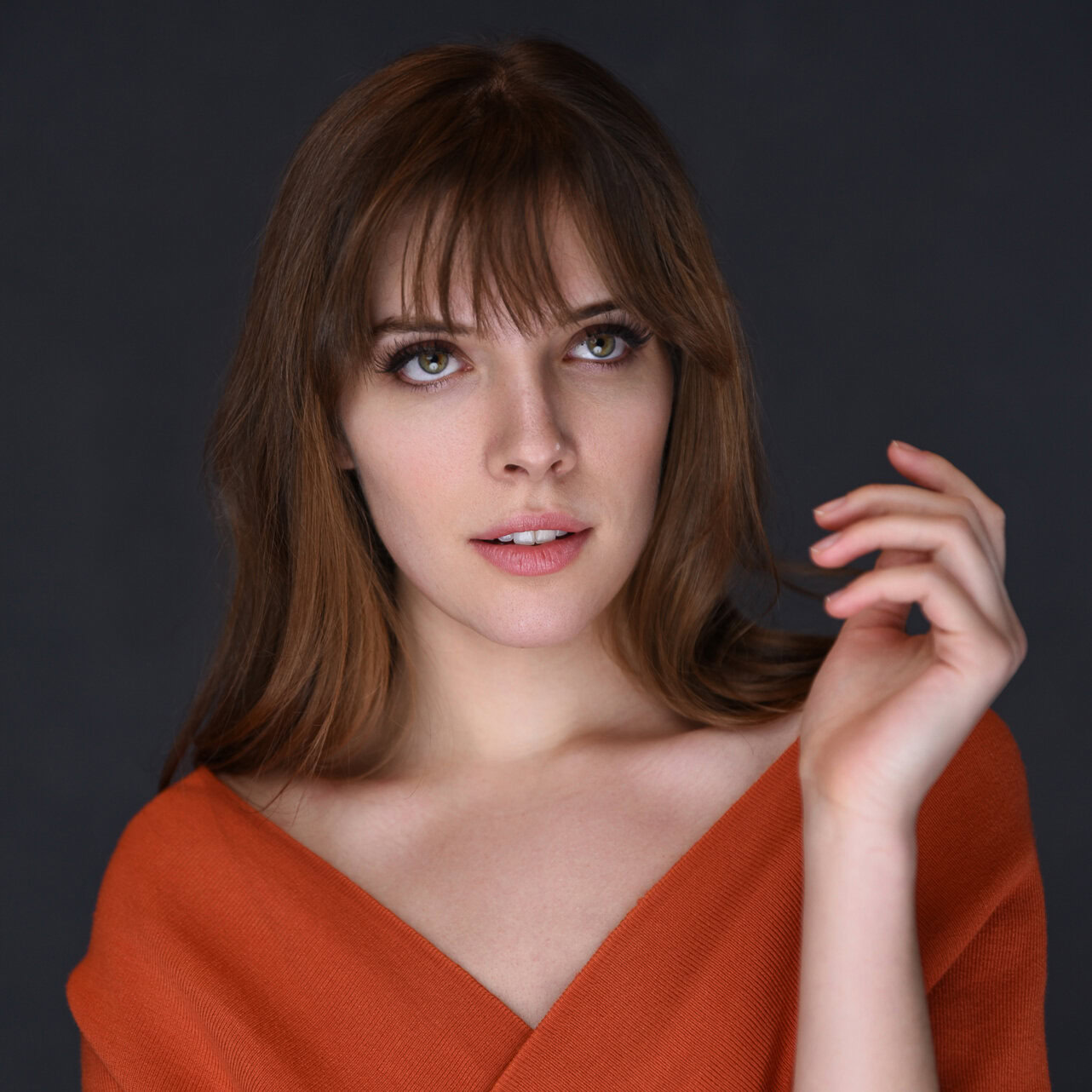 Professional Headshot a woman with long brown hair in an orange off-the-shoulder top, set against a dark backdrop.